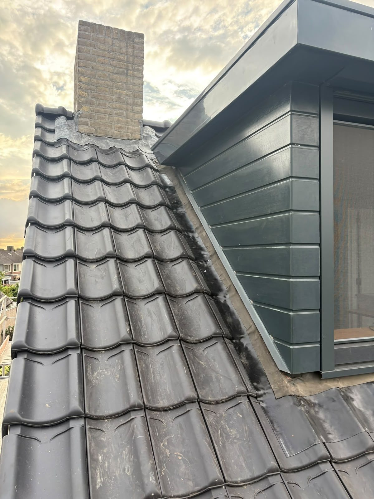 Nieuwe zwarte dakpannen tussen schoorsteen en dakkapel